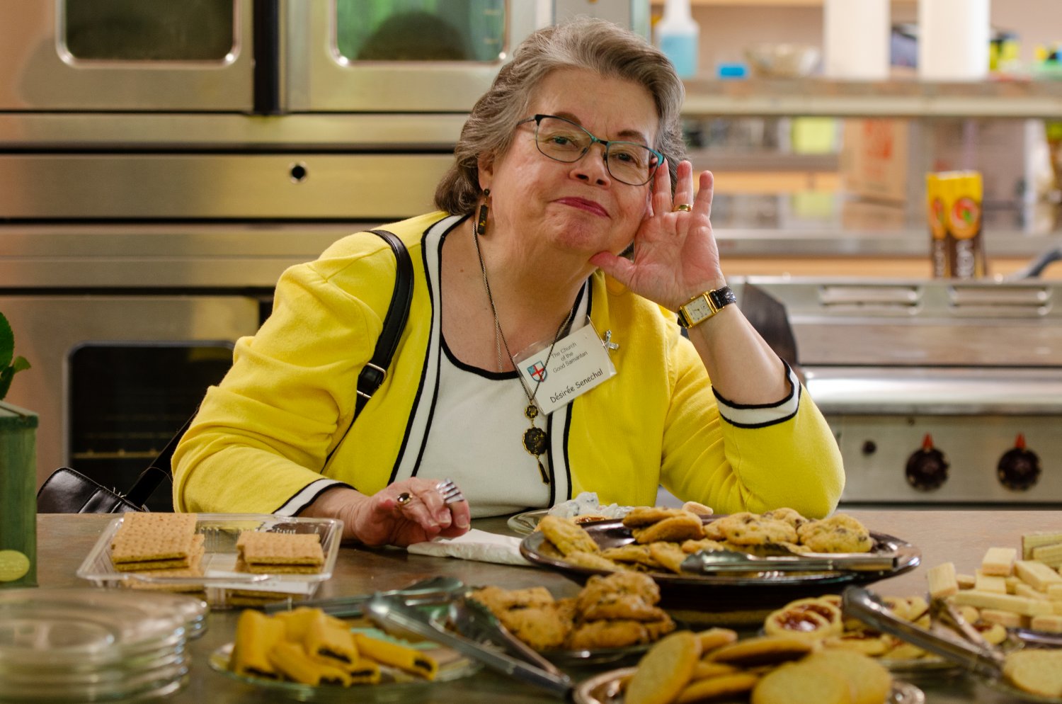 Woman in a yellow sweater hosts goodies at coffee hour