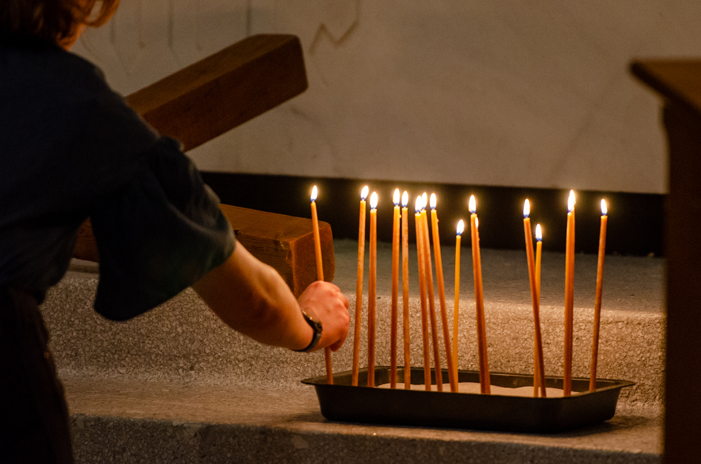 A hand reaches to take from a tray of lit candles