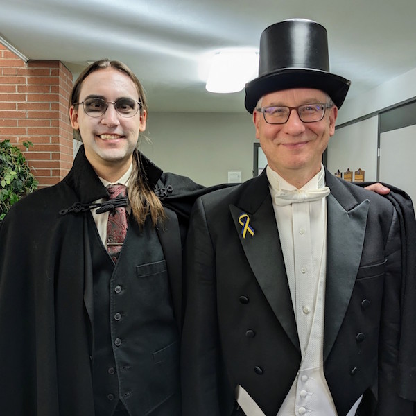 Two musicians in costume, one with a top hat, one with shadowy eyes