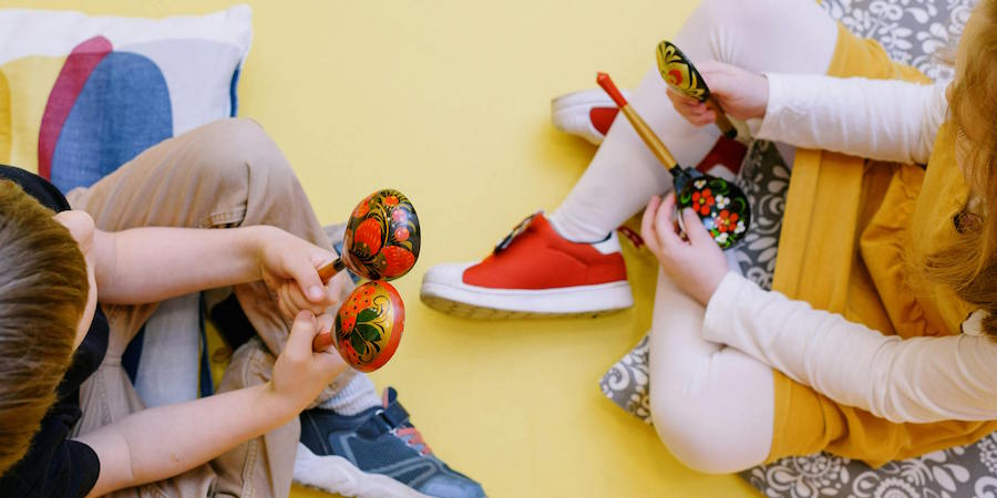 Birds-eye view of two children sitting on yellow floor, holding musical shakers