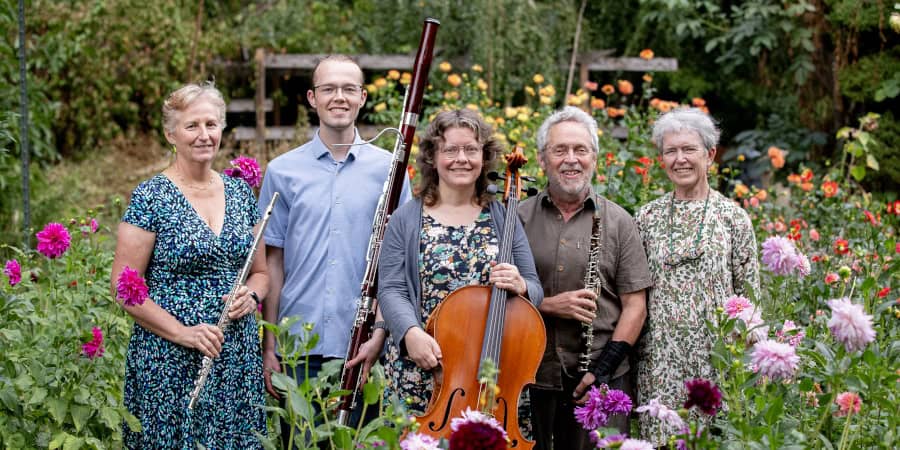 Group of five people with musical instruments in a colorful garden setting.