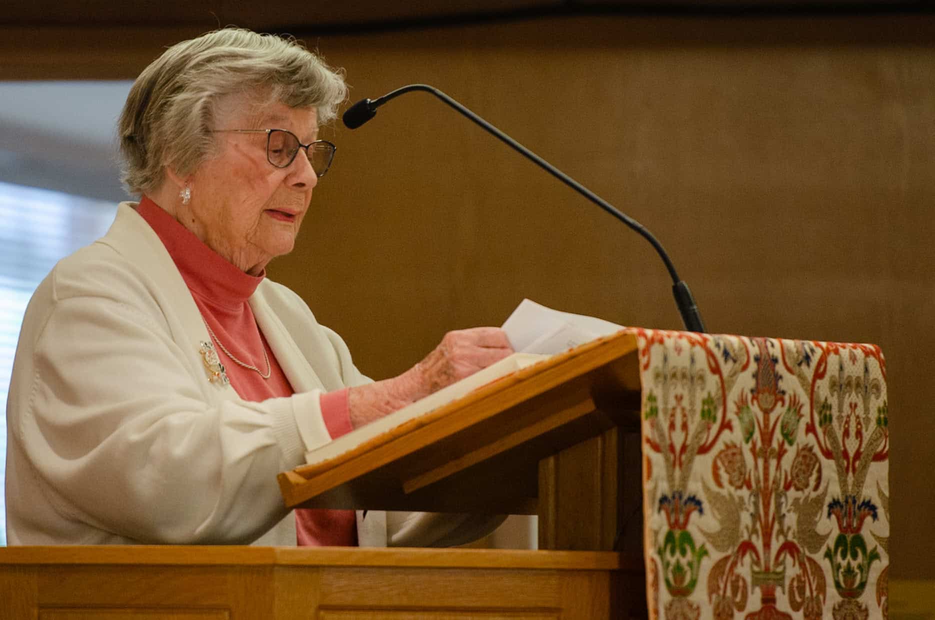 Elderly woman speaking at church podium during service.