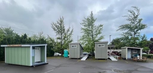 Small church buildings and portable restrooms in parking lot.