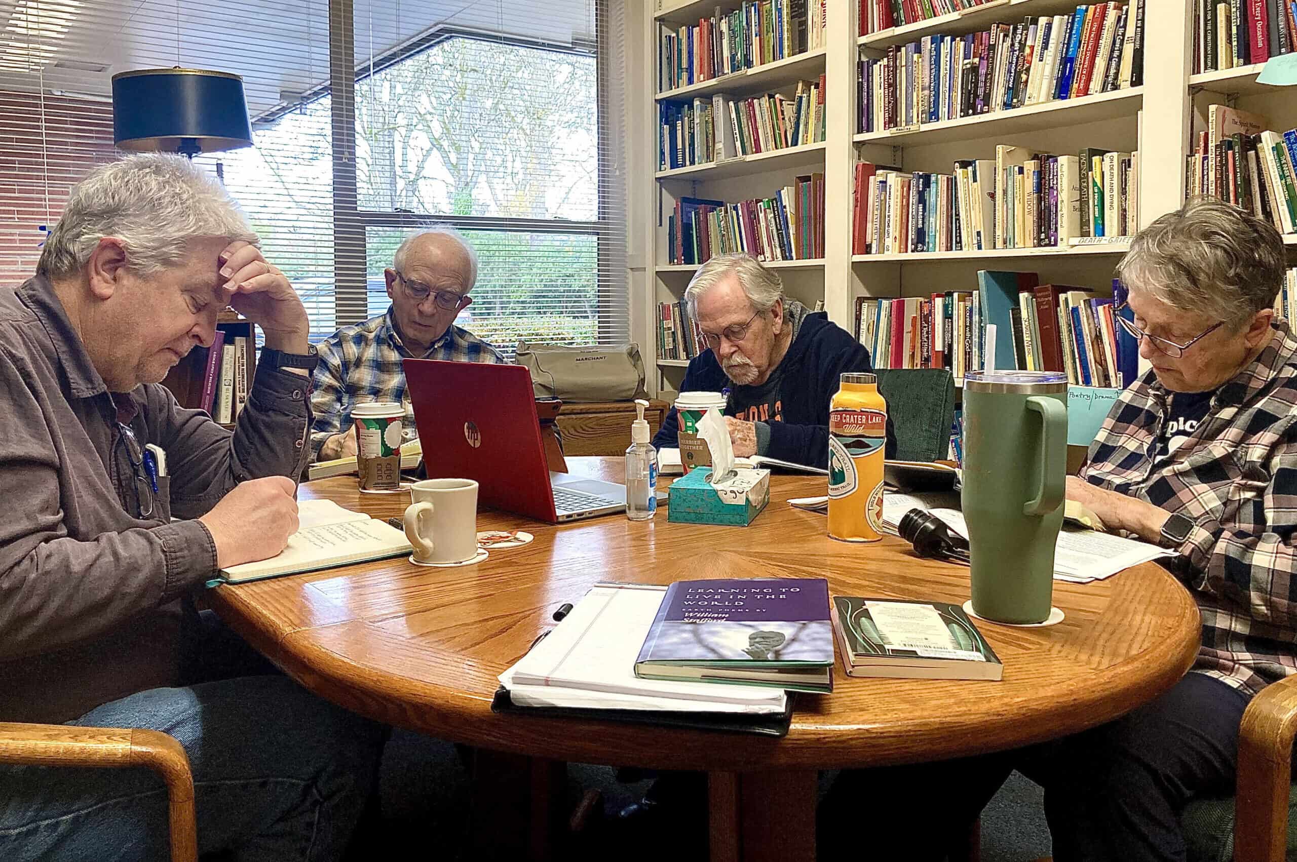 Group of seniors studying and discussing at a round table in a library.