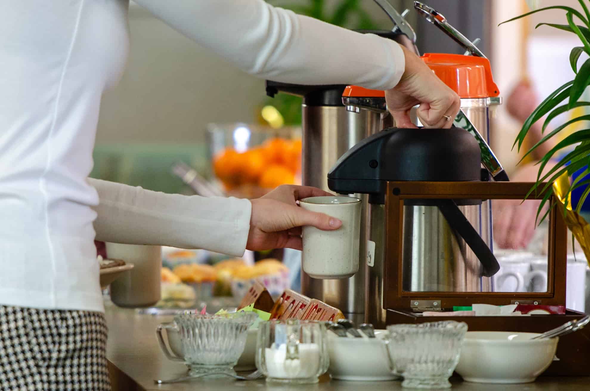 Person pouring milk at a breakfast buffet with cereal and bowls.